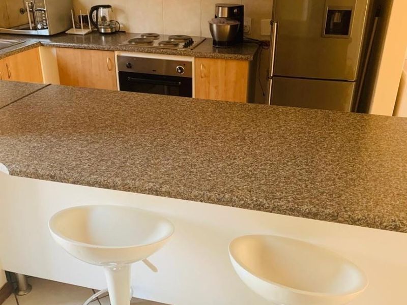 A functional kitchen featuring light wood cabinetry, granite countertops, a breakfast bar, and built-in cooking appliances with tiled flooring.