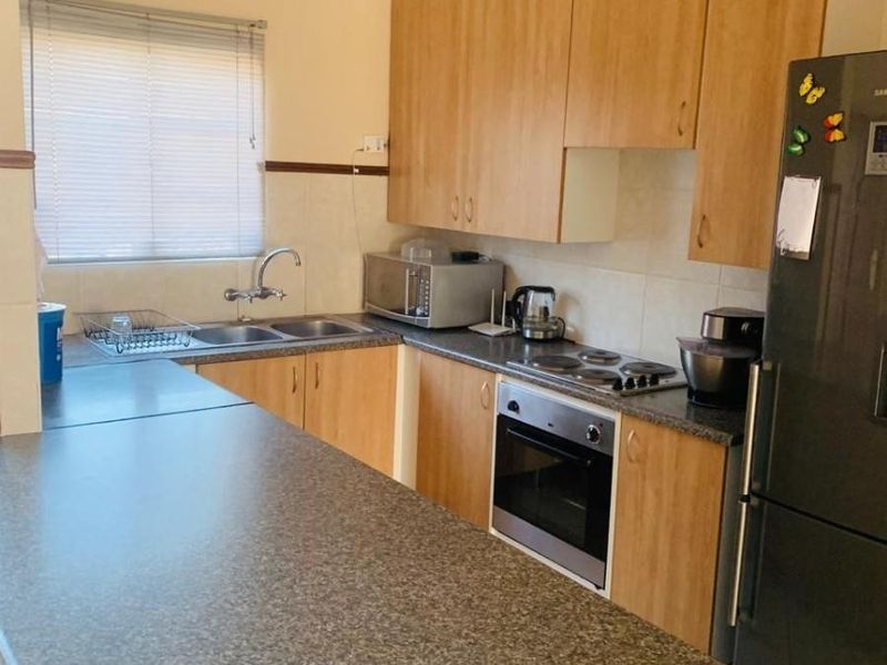 A functional kitchen featuring laminate cabinetry, granite-look countertops, a built-in oven, electric hob, and a stainless steel double sink with a tiled splashback.
