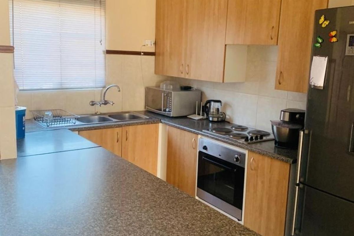 A functional kitchen featuring laminate cabinetry, granite-look countertops, a built-in oven, electric hob, and a stainless steel double sink with a tiled splashback.