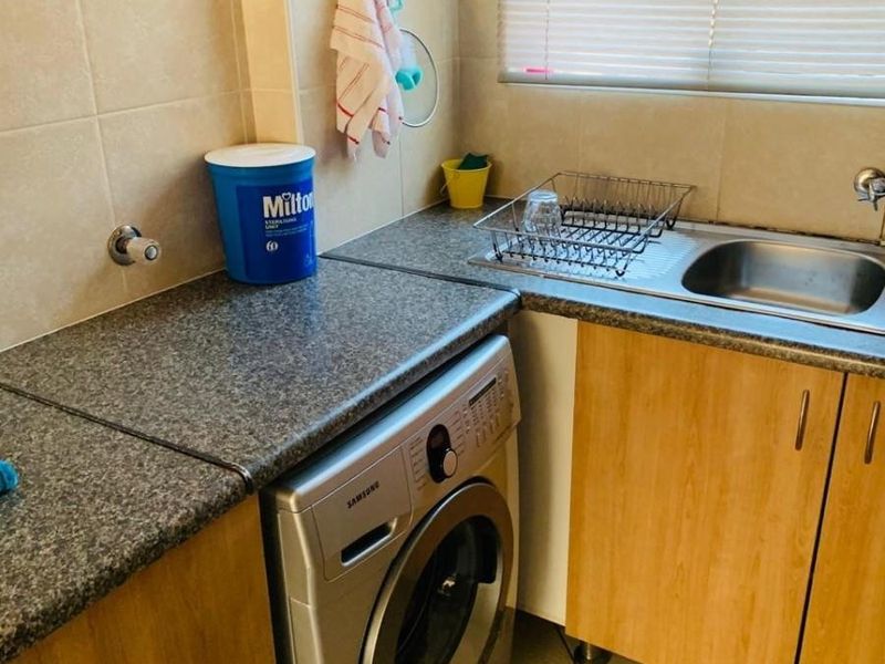 A functional laundry area featuring laminate cabinetry, granite countertops, a stainless steel sink, and tiled flooring with integrated plumbing for a washing machine.