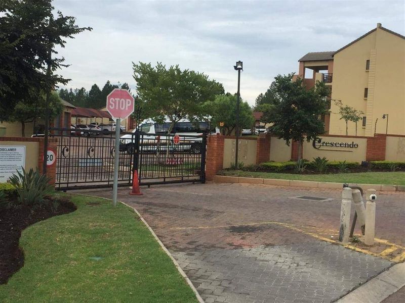 The main entrance to the Crescendo apartment complex, featuring a secure gated access point, brick boundary walls, and paved driveway.