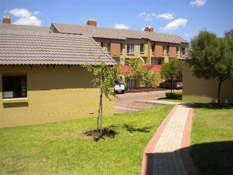 Exterior view of the apartment complex featuring a paved walkway, landscaped garden areas, and traditional tiled roofing.