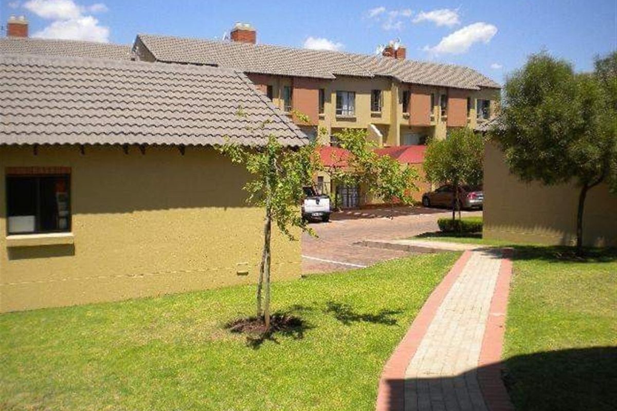 Exterior view of the apartment complex featuring a paved walkway, landscaped garden areas, and traditional tiled roofing.