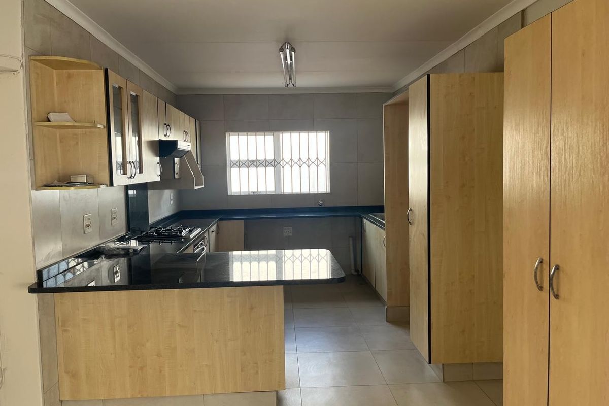 A functional kitchen featuring light wood cabinetry, dark granite countertops, a gas hob, and tiled finishes throughout.
