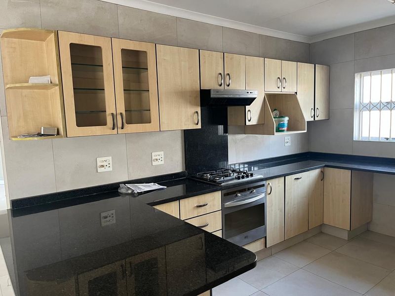 A functional kitchen featuring granite countertops, built-in oven, gas hob, extractor fan, and ample cabinetry with a neutral tiled finish.