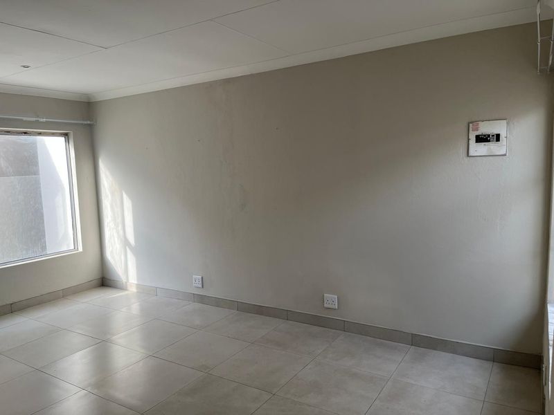An empty living area featuring neutral tiled flooring, wall-mounted electrical distribution board, and standard electrical outlets, ready for personalization.