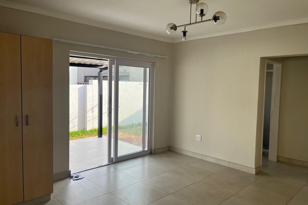 A bright, empty living area featuring tiled floors, a built-in cupboard, and a sliding glass door providing direct access to the outdoor patio.