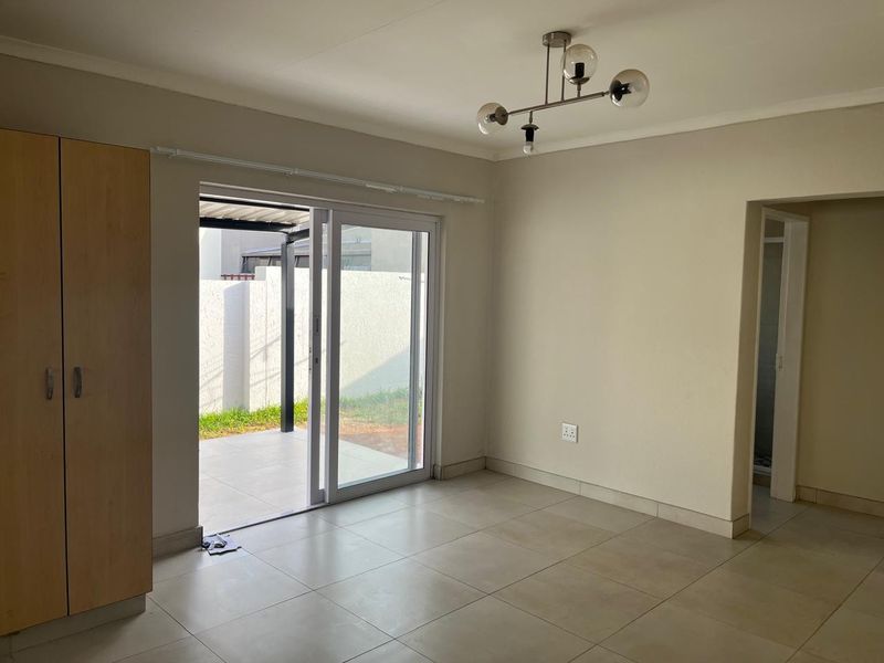 A bright, empty living area featuring tiled floors, a built-in cupboard, and a sliding glass door providing direct access to the outdoor patio.