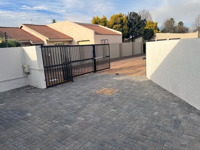 A paved driveway leading to a secure metal gate, featuring perimeter walls and a tiled roof structure.