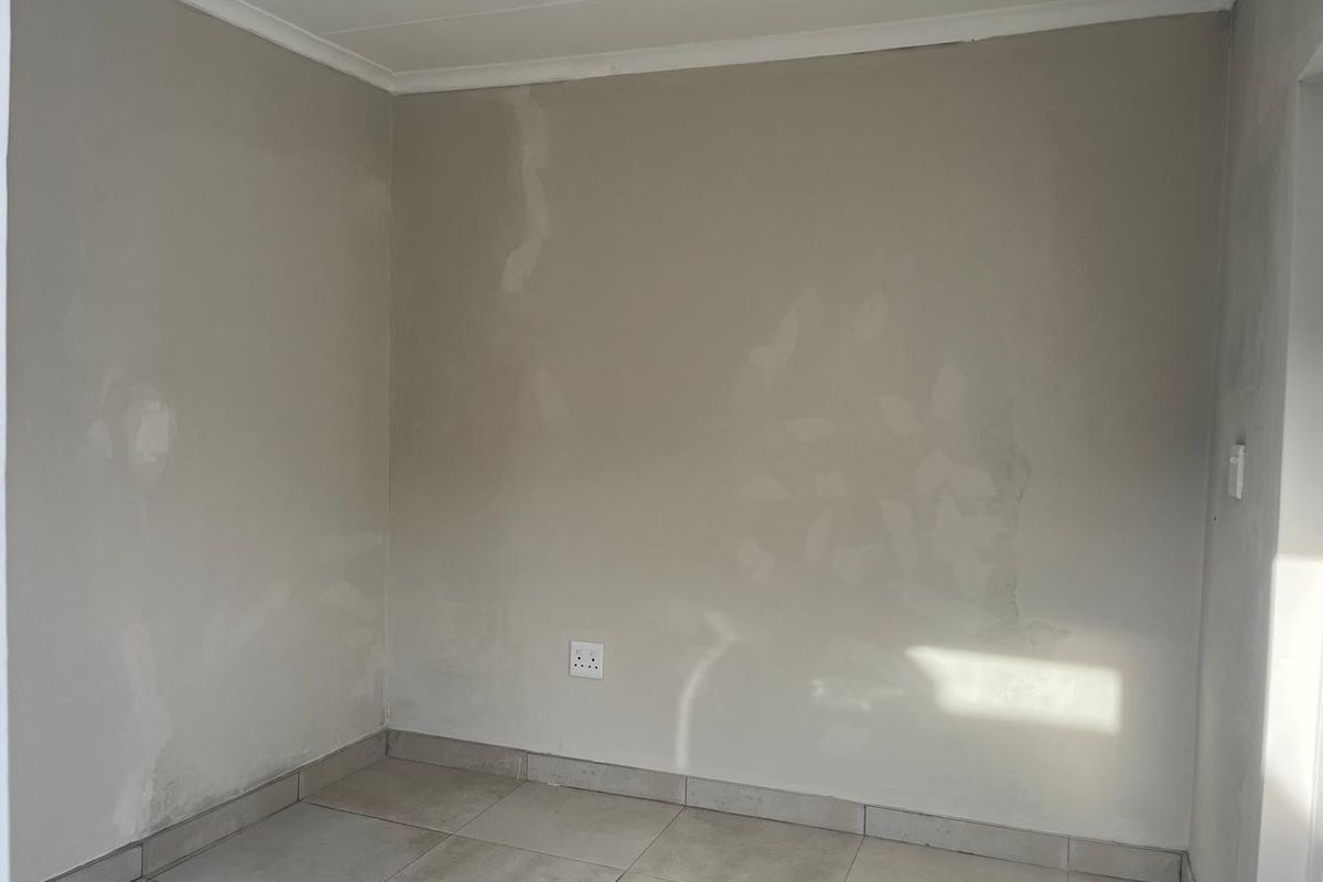 An empty bedroom featuring tiled flooring and walls requiring final painting and finishing touches.