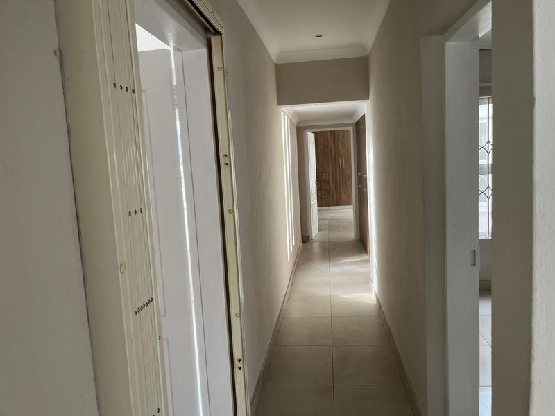 A neutral-toned hallway featuring tiled flooring, recessed lighting, and access to adjacent rooms with built-in storage cupboards.