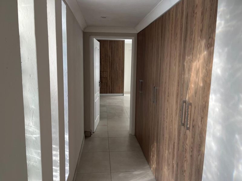 A clean, modern hallway featuring neutral tiled flooring and extensive built-in wooden cabinetry, leading through to an adjacent room.