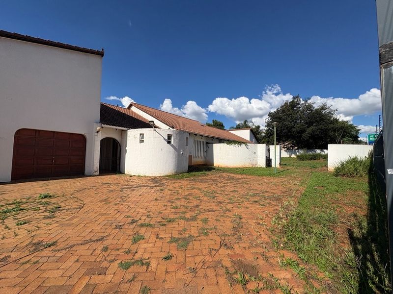 Front exterior view of the property featuring a paved driveway, garage access, and boundary walls with a tiled roof structure.