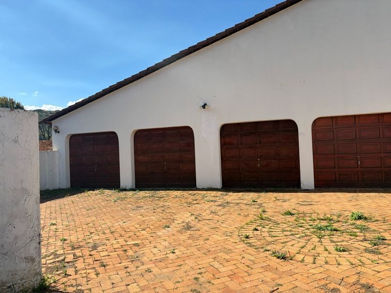 A triple garage featuring wooden doors and a brick-paved driveway, showing some signs of exterior wear and maintenance needs.