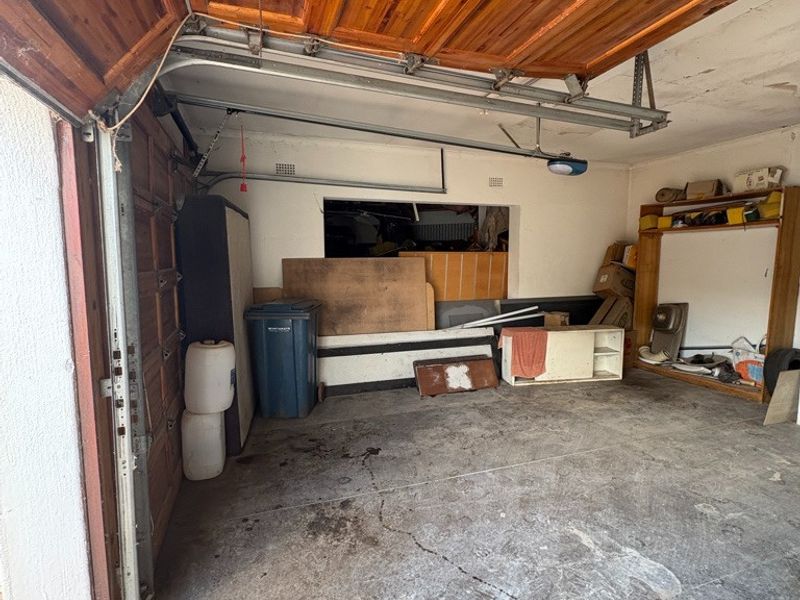 A functional garage space featuring a timber sectional door, concrete flooring, and built-in shelving, offering ample storage potential.