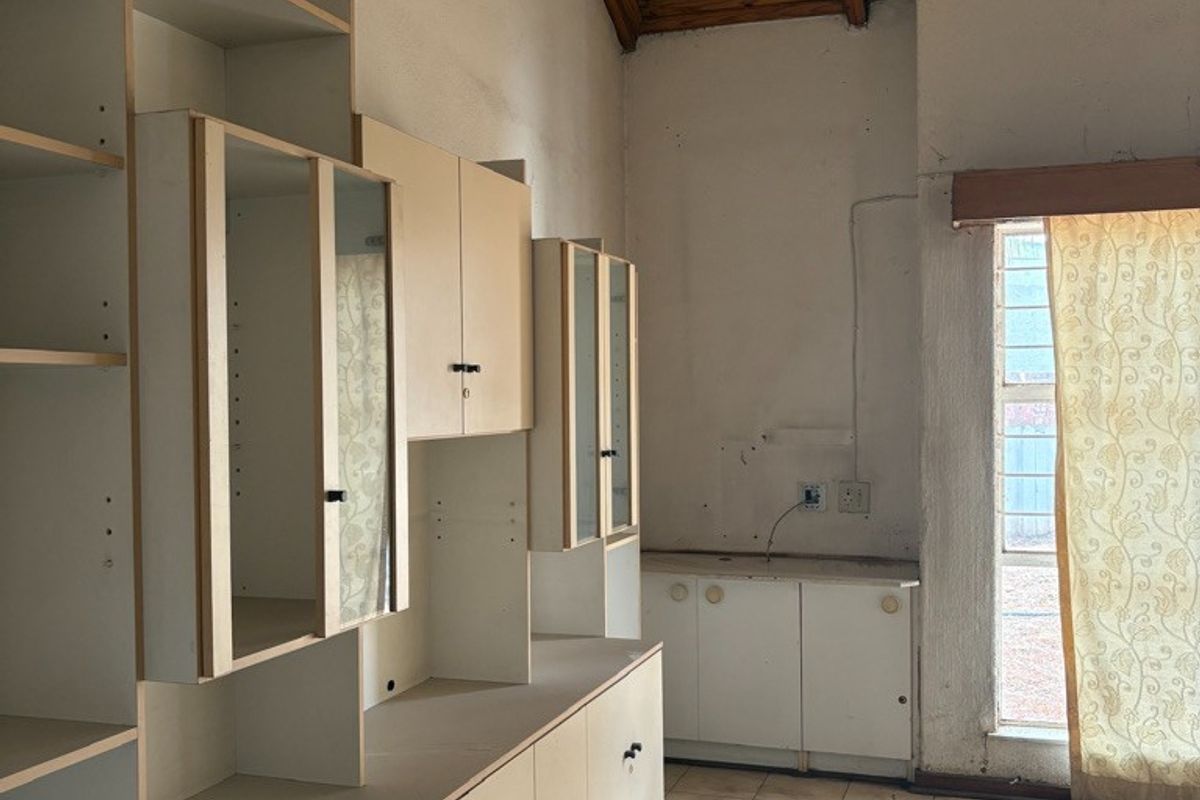 A dated kitchen area featuring built-in cabinetry, tiled flooring, and an exposed timber ceiling, offering significant potential for renovation and modernization.
