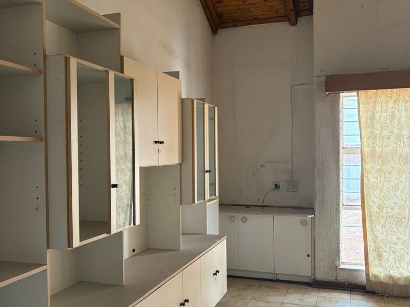 A dated kitchen area featuring built-in cabinetry, tiled flooring, and an exposed timber ceiling, offering significant potential for renovation and modernization.