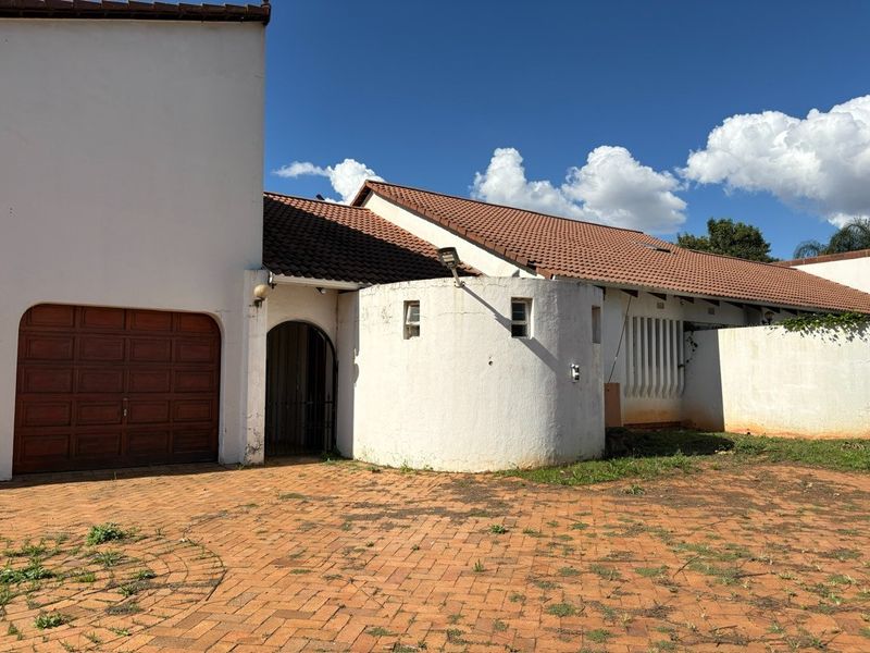 Front exterior view of the property featuring a tiled roof, arched entrance, garage, and a brick-paved driveway with some maintenance required on exterior finishes.