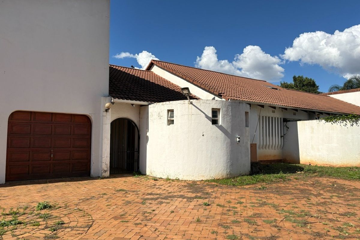 Front exterior view of the property featuring a tiled roof, arched entrance, garage, and a brick-paved driveway with some maintenance required on exterior finishes.