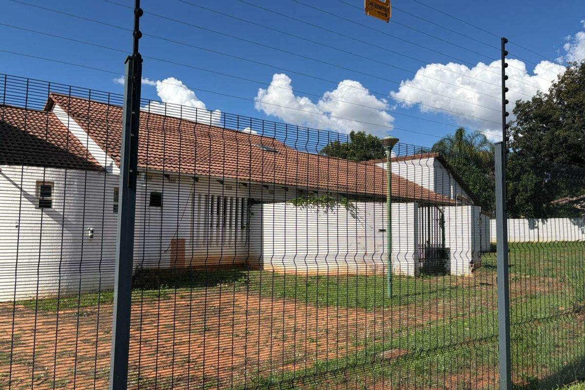 Rear exterior view of the property featuring a tiled roof, security fencing, and a paved yard area.