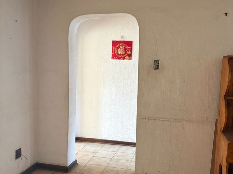 An empty living area featuring a timber ceiling, ceramic tiled flooring, and a distinctive arched doorway leading to an adjacent space.