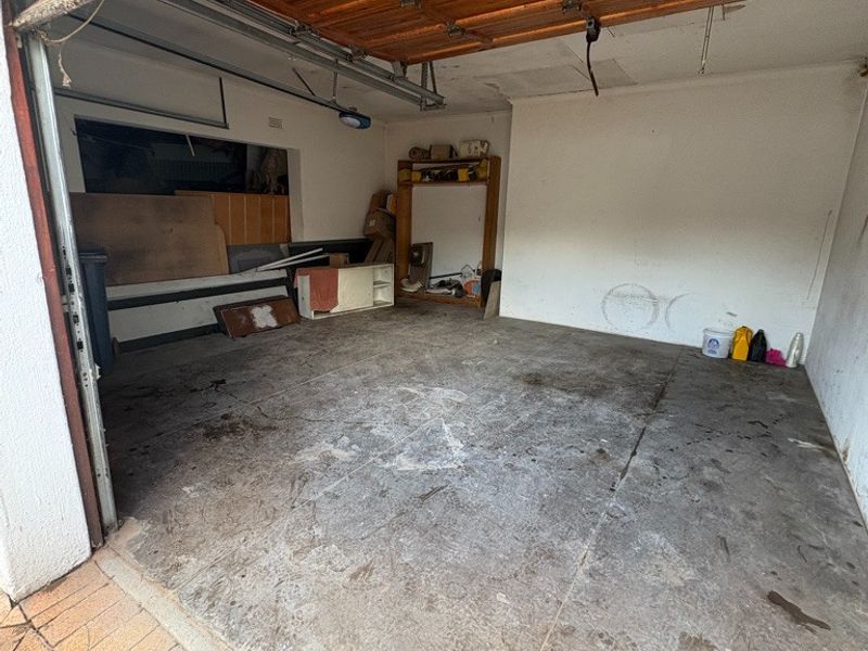 A spacious, empty garage featuring a sectional door, exposed timber ceiling, and concrete flooring, requiring maintenance and cosmetic updates.