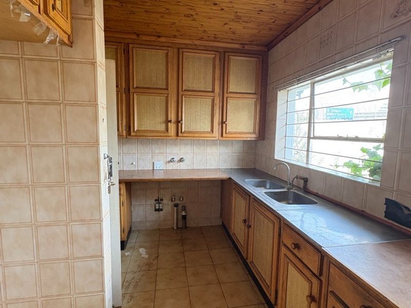 A dated kitchen featuring wooden cabinetry, tiled splashbacks, and a double basin sink, offering a functional layout ready for modern renovation.