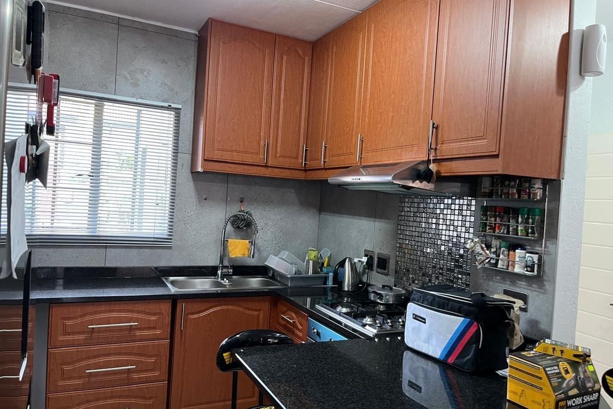A functional kitchen featuring wood-look cabinetry, granite countertops, a gas hob with extractor fan, and a mosaic tile splashback.