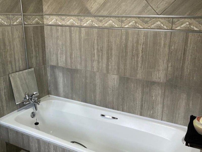 A clean bathroom featuring a built-in bathtub with a handheld shower mixer and neutral-toned decorative wall tiling.