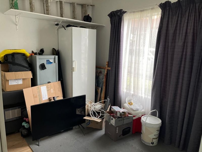 A utility or storage room featuring wall-mounted shelving and a window with curtains, currently used for general storage.