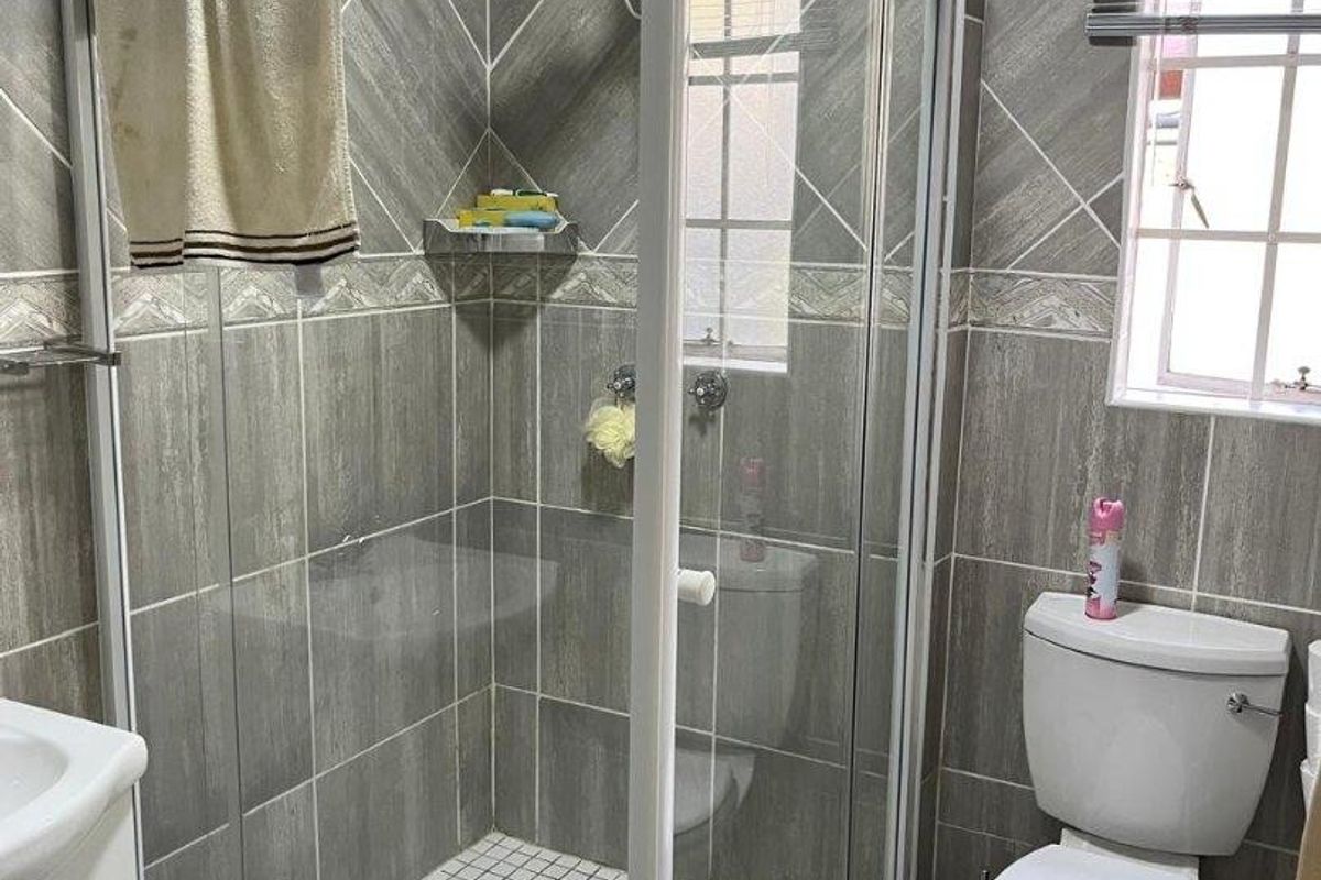 A functional bathroom featuring a corner shower enclosure, tiled walls, a standard toilet, and a vanity basin with natural light from a window.