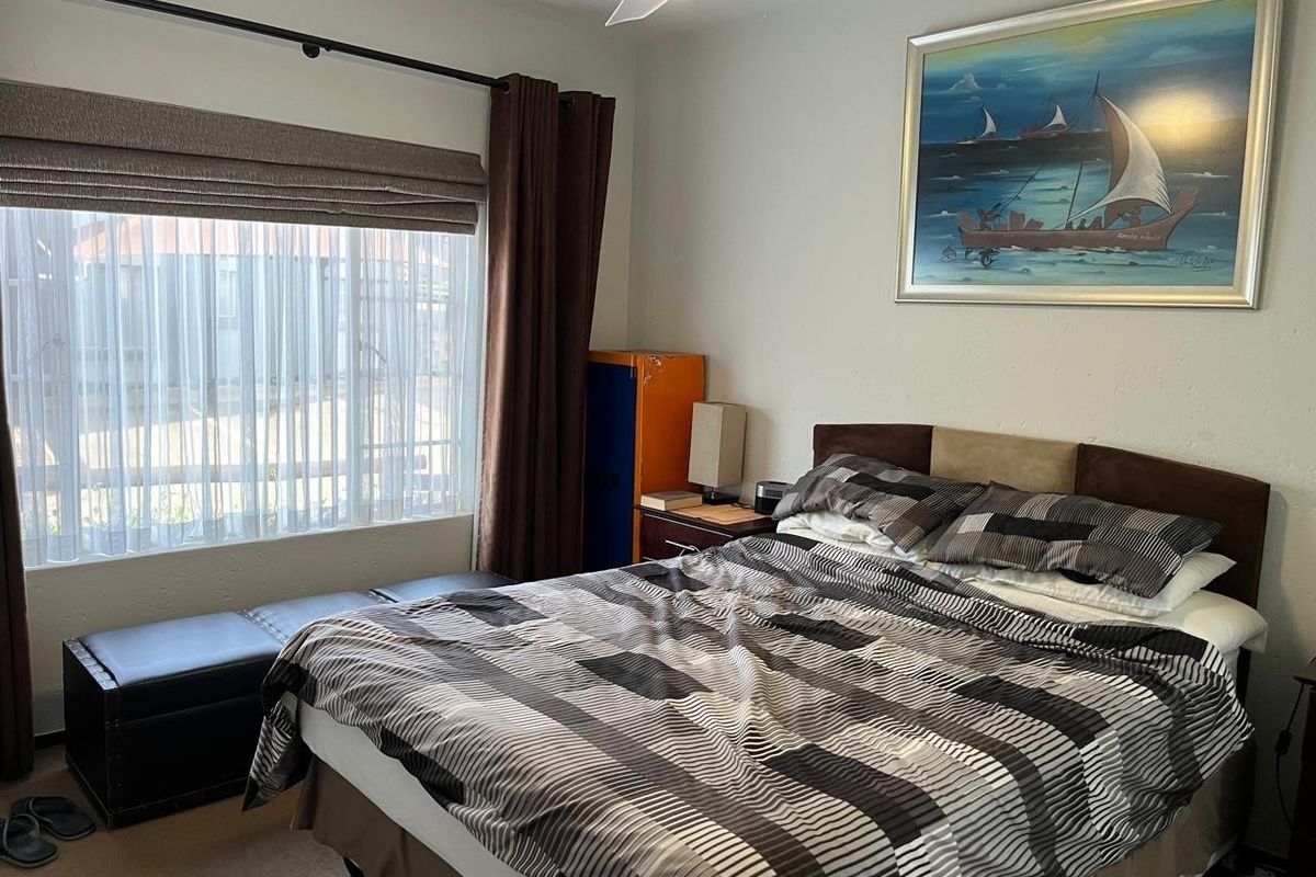 A functional bedroom featuring a ceiling fan, large window with fitted curtain rod, and neutral wall finishes.