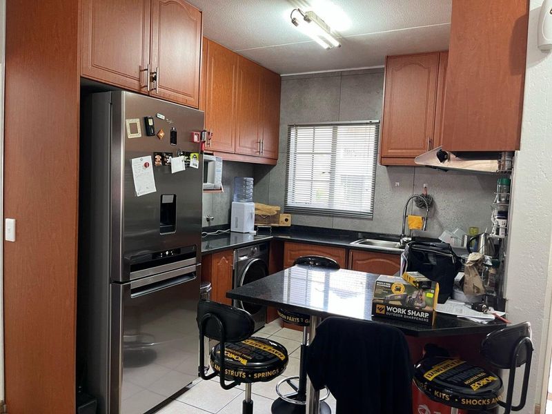 Functional kitchen featuring wood-look cabinetry, granite countertops, integrated sink, and tiled flooring, providing a practical workspace with ample storage.