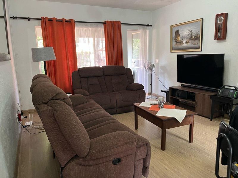 A comfortable living room featuring light-toned laminate flooring and access to the outdoor area through a glass sliding door.