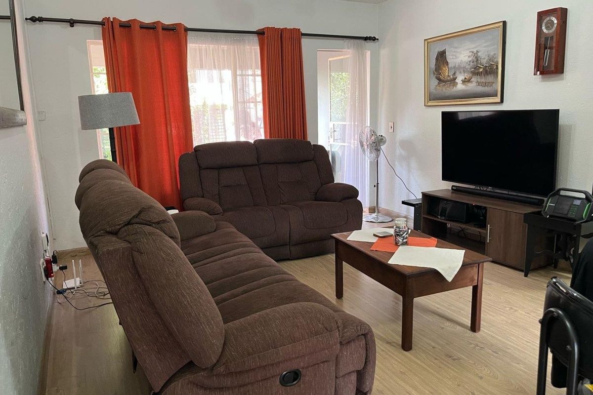 A comfortable living room featuring light-toned laminate flooring and access to the outdoor area through a glass sliding door.