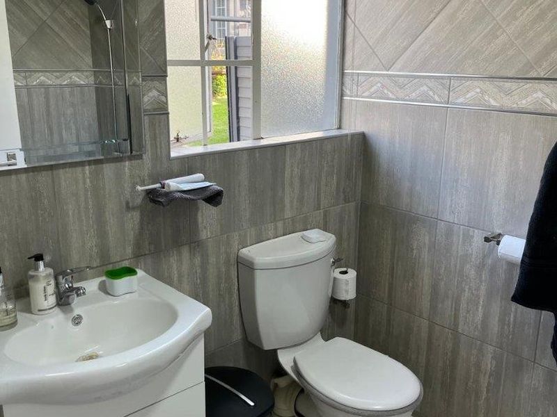 A compact bathroom featuring floor-to-ceiling grey tiling, a white vanity cabinet with a basin, and a standard toilet.