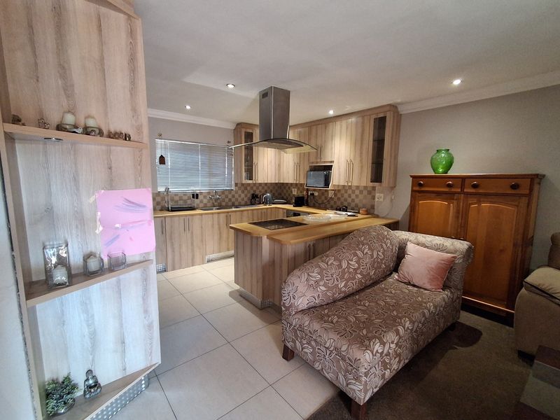 Open-plan kitchen featuring light wood-finish cabinetry, a central hob with extractor fan, and tiled flooring, seamlessly integrated with the living area.