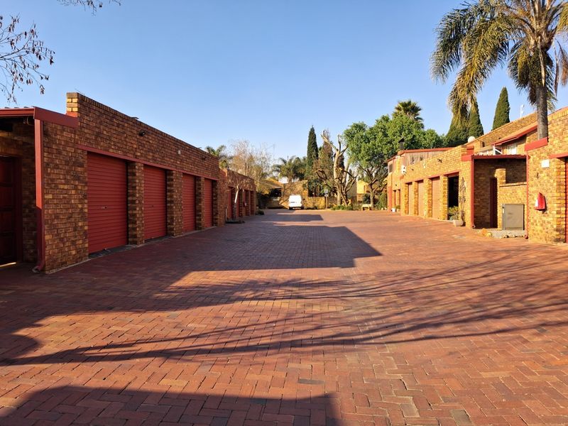 A view of the townhouse complex driveway featuring multiple garage units with red roller doors and traditional face brick construction.