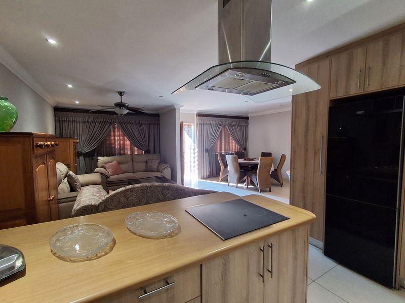 Open-plan living area featuring a kitchen with island, built-in cabinetry, and integrated hob, flowing into a dining and lounge space with tiled flooring.