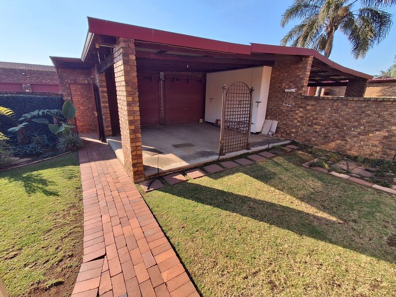 Open-style brick garage with built-in storage cabinetry, concrete flooring, and an adjacent paved walkway leading through the garden area.