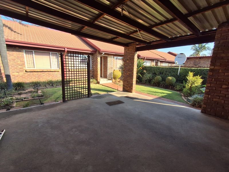 A covered carport area with a concrete driveway, brick facade, and access to the front entrance of the townhouse.