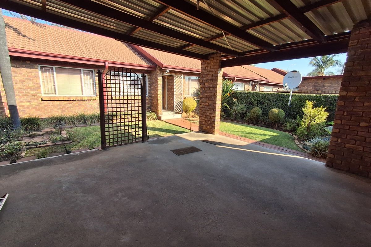 A covered carport area with a concrete driveway, brick facade, and access to the front entrance of the townhouse.