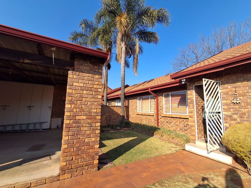 A well-maintained rear exterior view of a face brick townhouse featuring a covered patio, paved walkway, and established garden area.