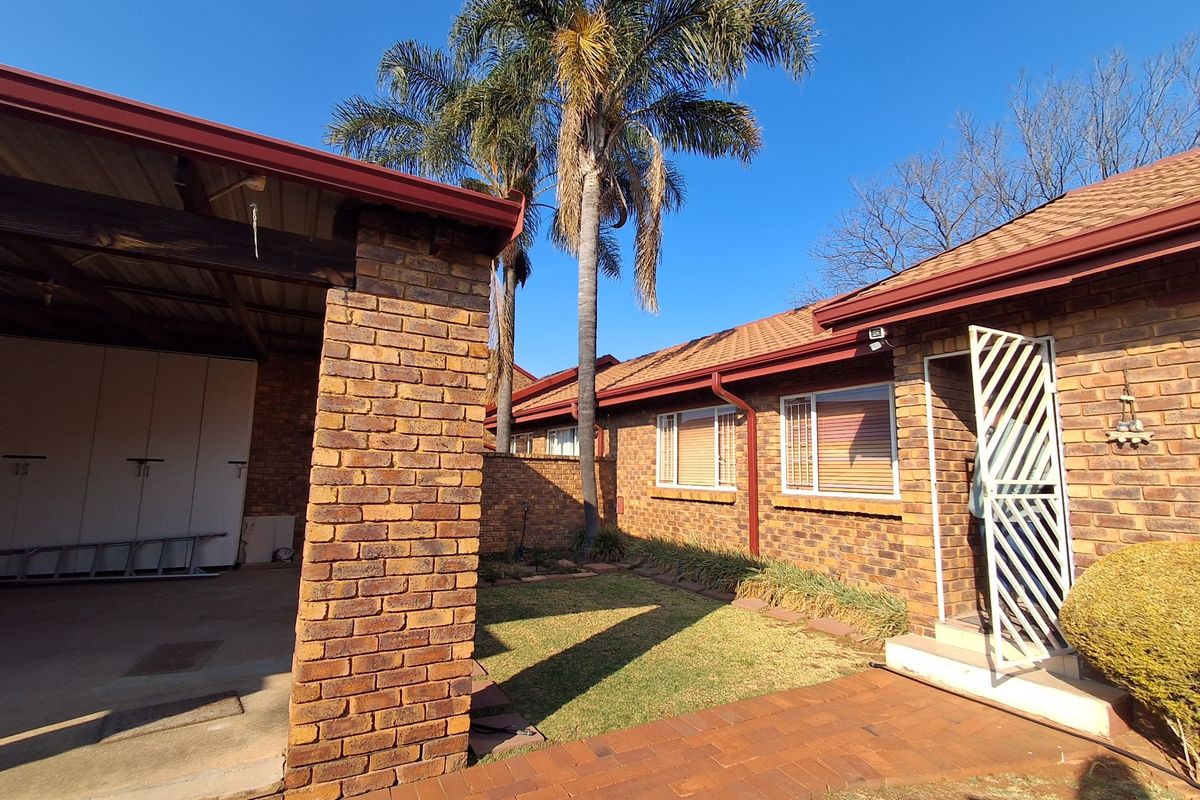 A well-maintained rear exterior view of a face brick townhouse featuring a covered patio, paved walkway, and established garden area.