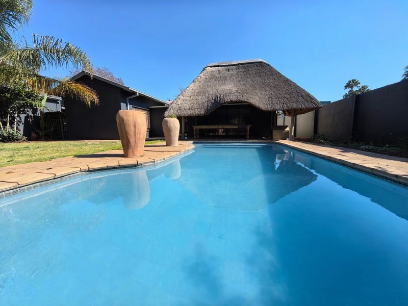 A well-maintained swimming pool area featuring a traditional thatched lapa, paved surround, and private boundary walls, perfect for outdoor relaxation and entertainment.