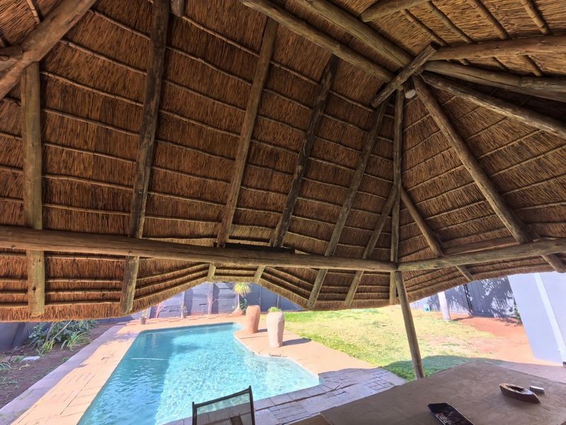 Outdoor entertainment area featuring a traditional thatch roof structure overlooking a swimming pool and garden.