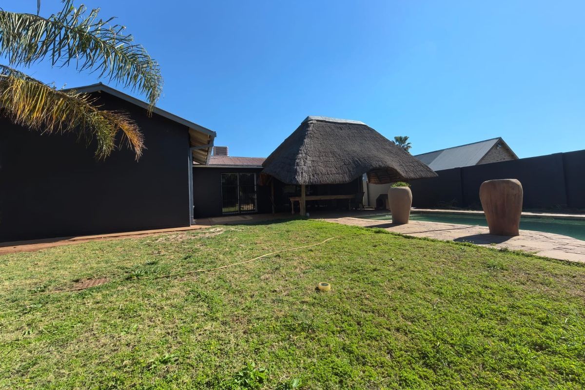 Rear garden area featuring a swimming pool, paved patio space, and a traditional thatched lapa structure.