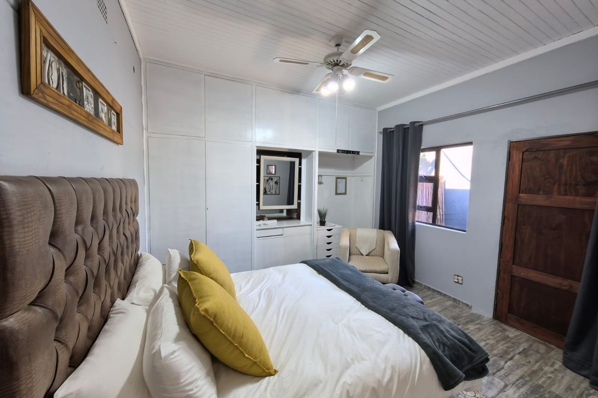 A bedroom featuring built-in cupboards, a ceiling fan, and timber-look flooring, offering a functional and comfortable living space.