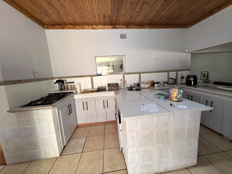 Functional kitchen featuring a gas hob, tiled countertops, a central island, and a distinctive timber tongue and groove ceiling.