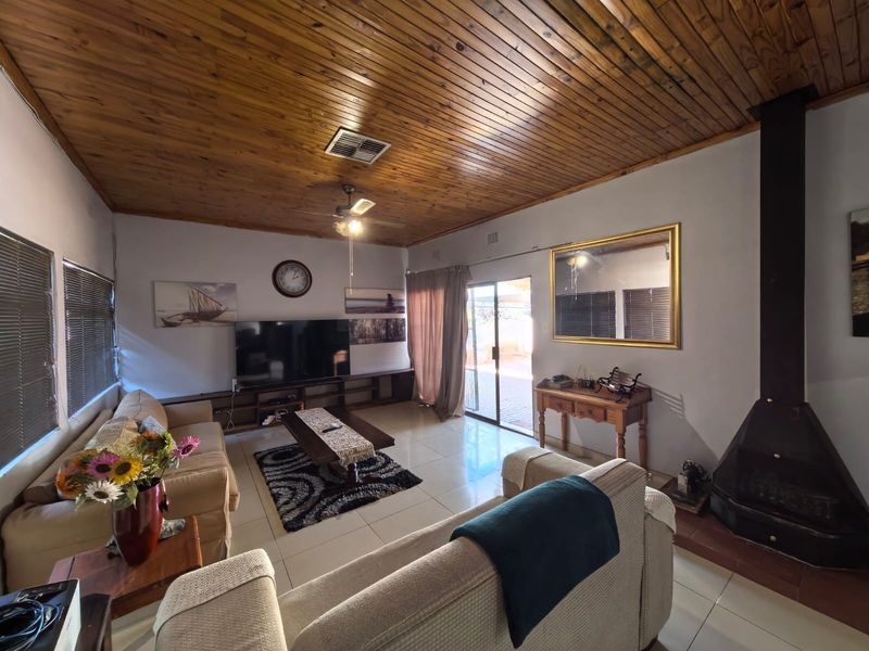 Spacious living room featuring a warm timber-clad ceiling, tiled flooring, and a cozy freestanding fireplace, with direct access to the outdoor area.
